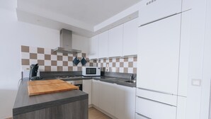 A modern kitchen with white cabinets, a microwave, and a wooden cutting board on the counter. - Apartment Nieuwpoort Near Beach Promenade (Koksijde)