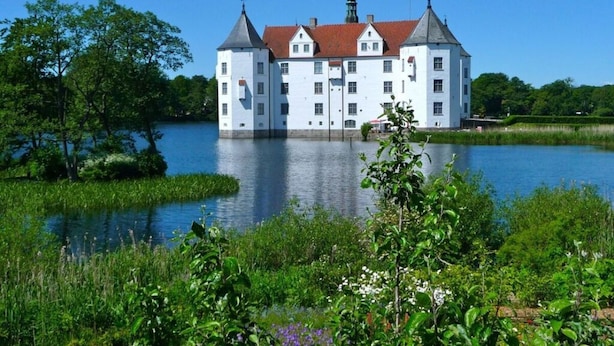 Un gran edificio blanco con múltiples torres, ubicado sobre un lago rodeado de vegetación.