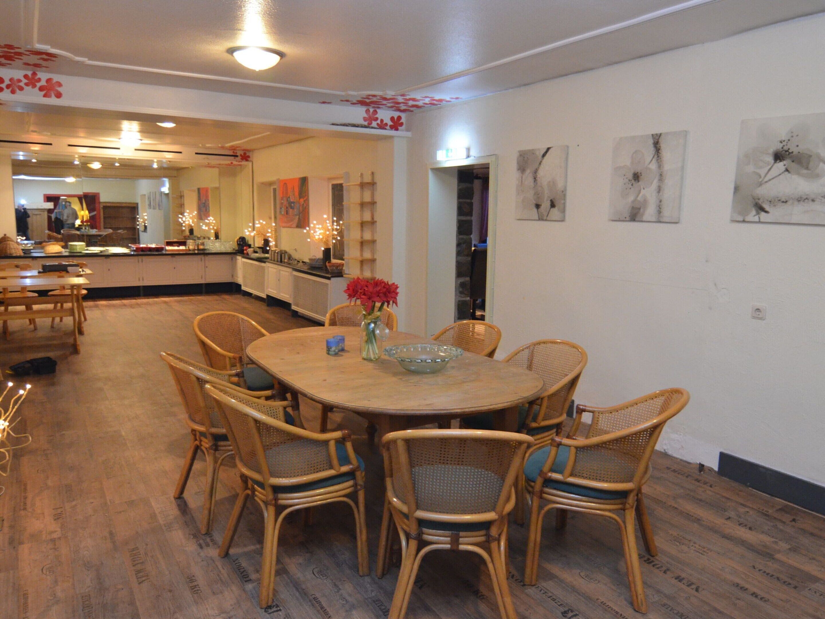 A dining area with a round wooden table, wicker chairs, and a vase with red flowers.