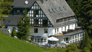 Un chalet traditionnel doté d’un toit à forte pente, d’un balcon et d’une terrasse avec des sièges d’extérieur.