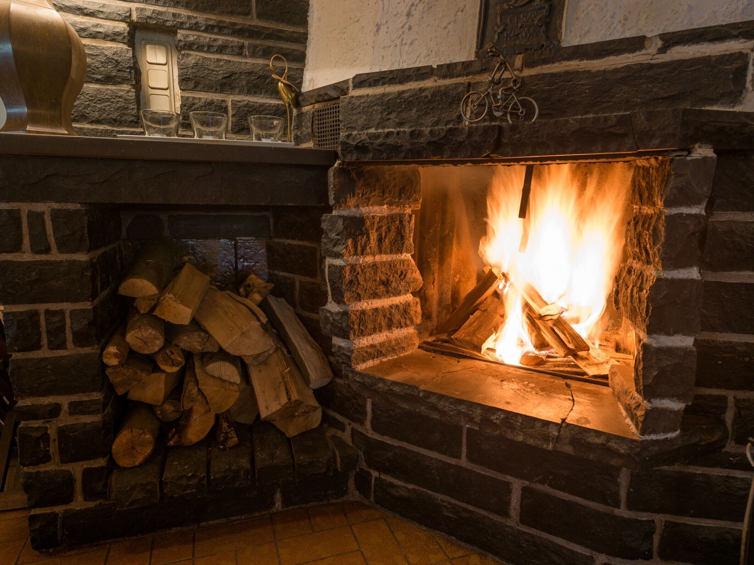 A stone fireplace with a fire, a stack of firewood, and a decorative metal piece.