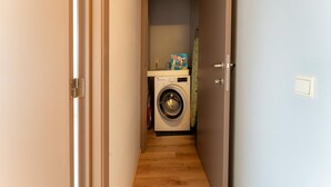 A narrow hallway with a washing machine and a box of detergent on a shelf. - Beachside Holiday Retreat in De Haan (De Haan)