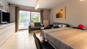 A modern hotel room with a dining area, a flat-screen TV, a large window with curtains, a painting on the wall, and a red chair. - Beachside Holiday Retreat in De Haan (De Haan)