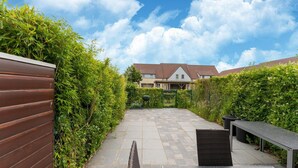 A courtyard with a paved patio, a wooden fence, and a building in the background. - Beachside Holiday Retreat in De Haan (De Haan)