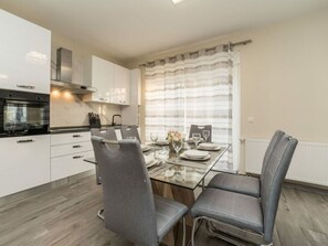 A modern kitchen with white cabinets, a black oven, and a stainless steel range hood. There is a dining table with two grey chairs and a vase of flowers. - Nicoll With Pool, 50 m From the Beach (Privlaka)