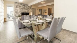Un espace repas moderne avec une table en verre, des chaises à revêtement gris et un mur d’accent en pierre.