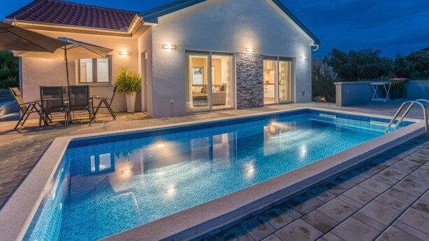 Une maison moderne dotée d’une piscine, de mobilier de jardin et d’un mur d’accent en pierre.
