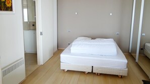 Une chambre à coucher avec un grand lit, une armoire et une salle de bain visible à travers une porte ouverte.