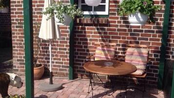 A brick building with a green pergola, a round table with chairs, and hanging planters.