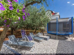 Un jardin avec un trampoline, un coin salon extérieur et un arbre aux fleurs violettes.