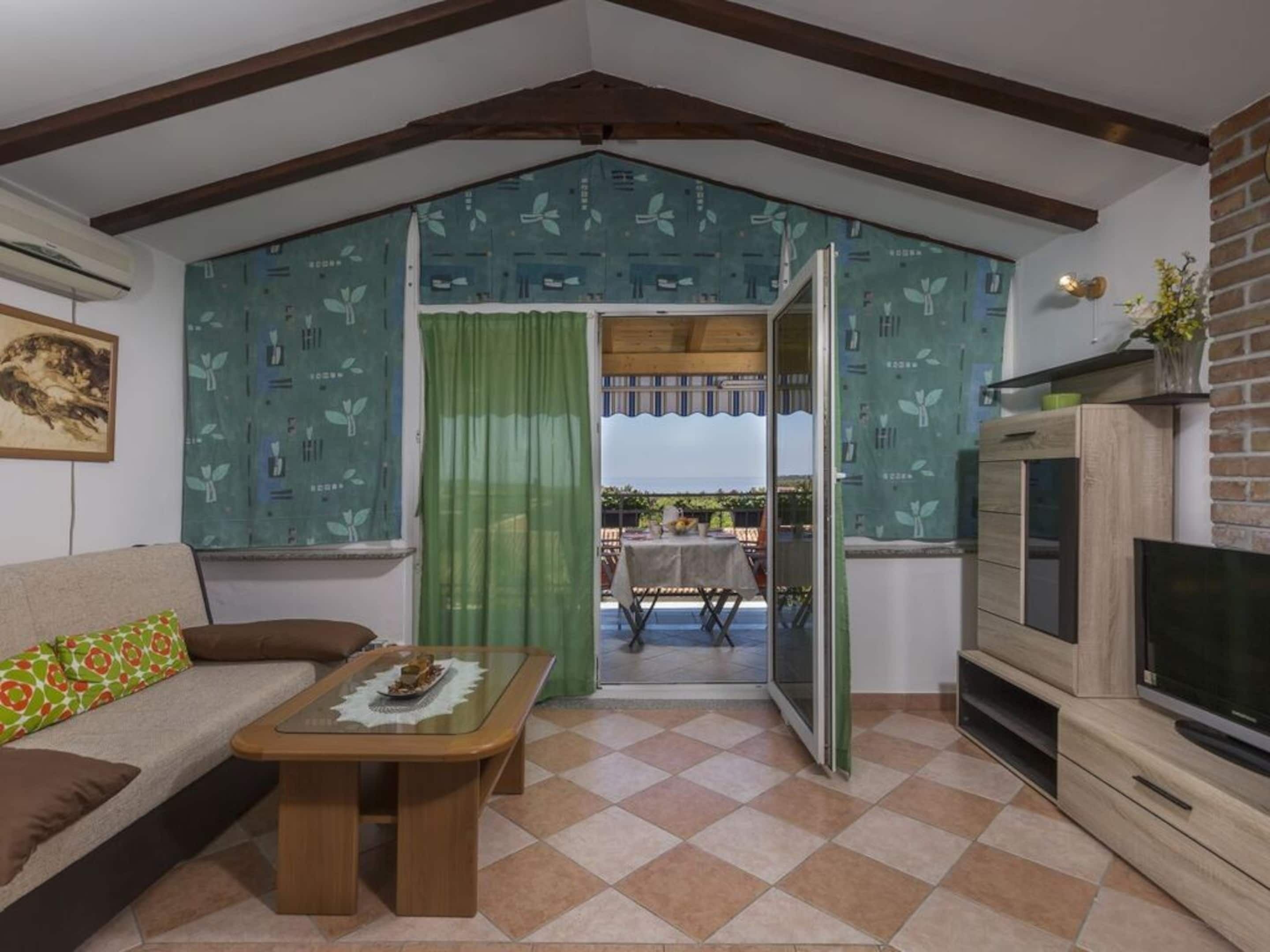 A cozy living room with a sofa, coffee table, and TV stand. A sliding glass door leads to an outdoor patio.