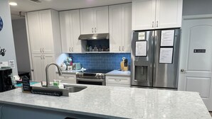 A modern kitchen with white cabinets, a stainless steel refrigerator, a built-in oven, and a marble countertop. - Hidden Gem near Lackland AFB, SeaWorld & Downtown Alamo (San Antonio)