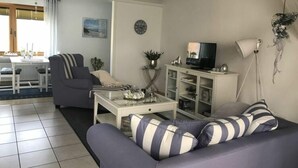 Uma sala de estar com sofá, mesa de centro, televisão e um espaço de jantar com mesa e cadeiras.