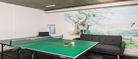 Una mesa de ping pong con red, un sofá y un mural en la pared.