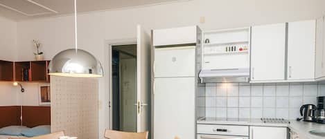 Una cucina compatta con mobili bianchi, forno integrato e macchina da caffè.