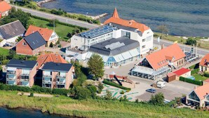 An aerial view of a coastal town with a mix of residential and commercial buildings, including a prominent hotel with a large glass facade and a restaurant with outdoor seating. - 4 Person Holiday Park Home in Hejls (Hejls)