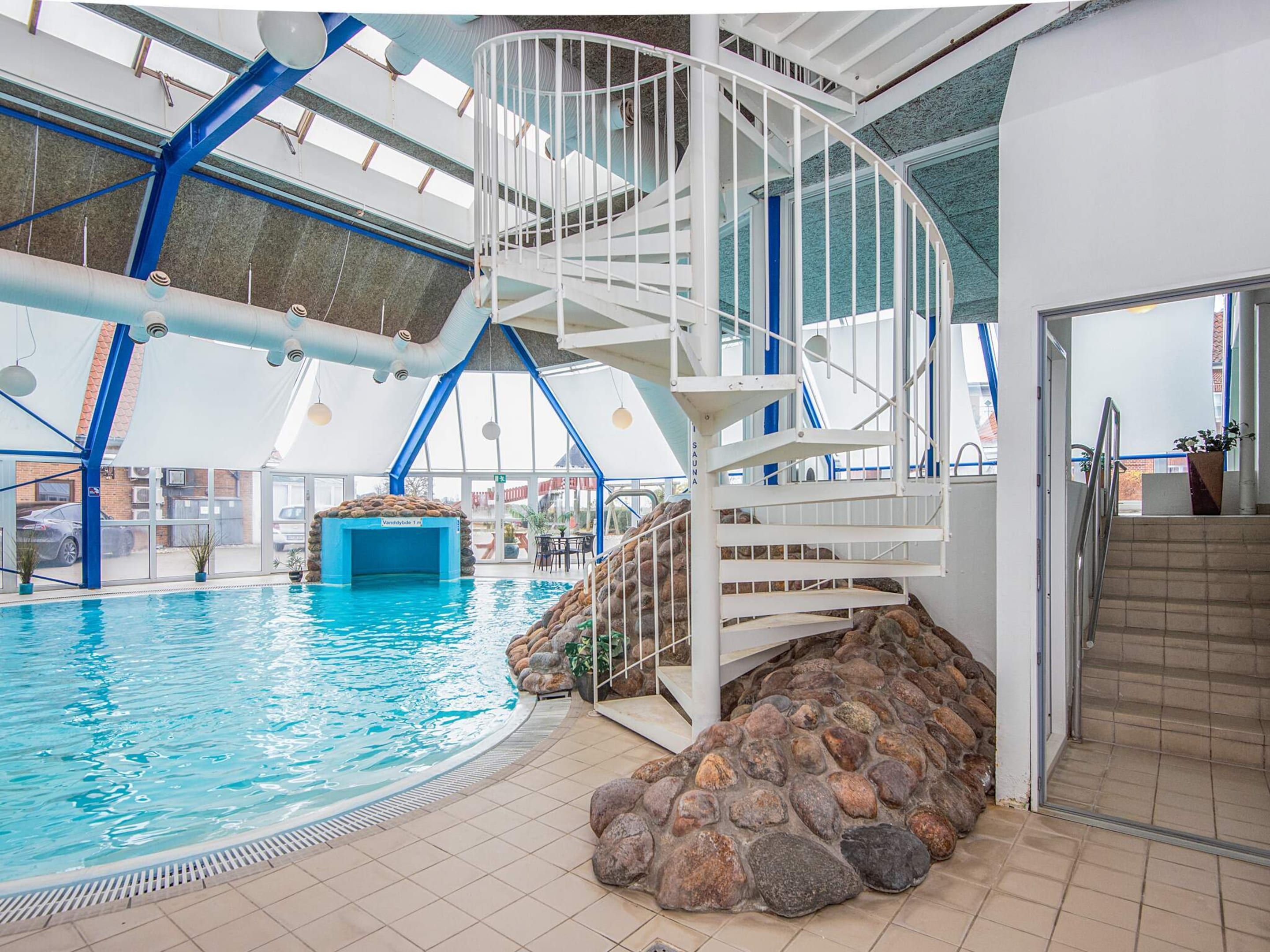 An indoor swimming pool with a white spiral staircase and a sauna area.