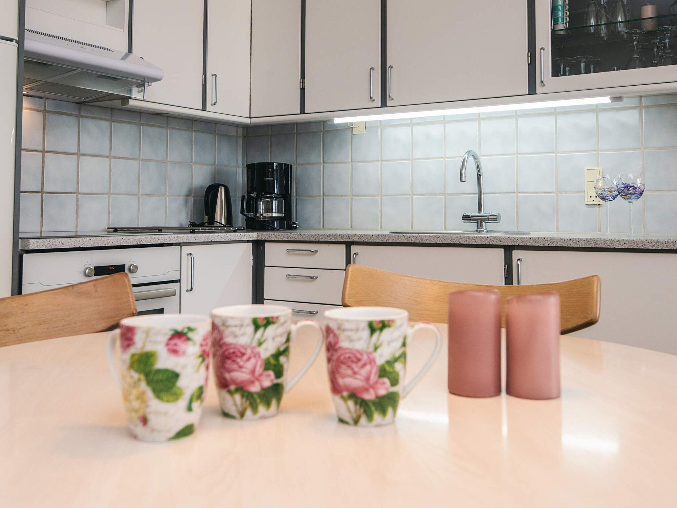 A kitchen with white cabinets, a coffee maker, and a sink. There are floral mugs on the table.
