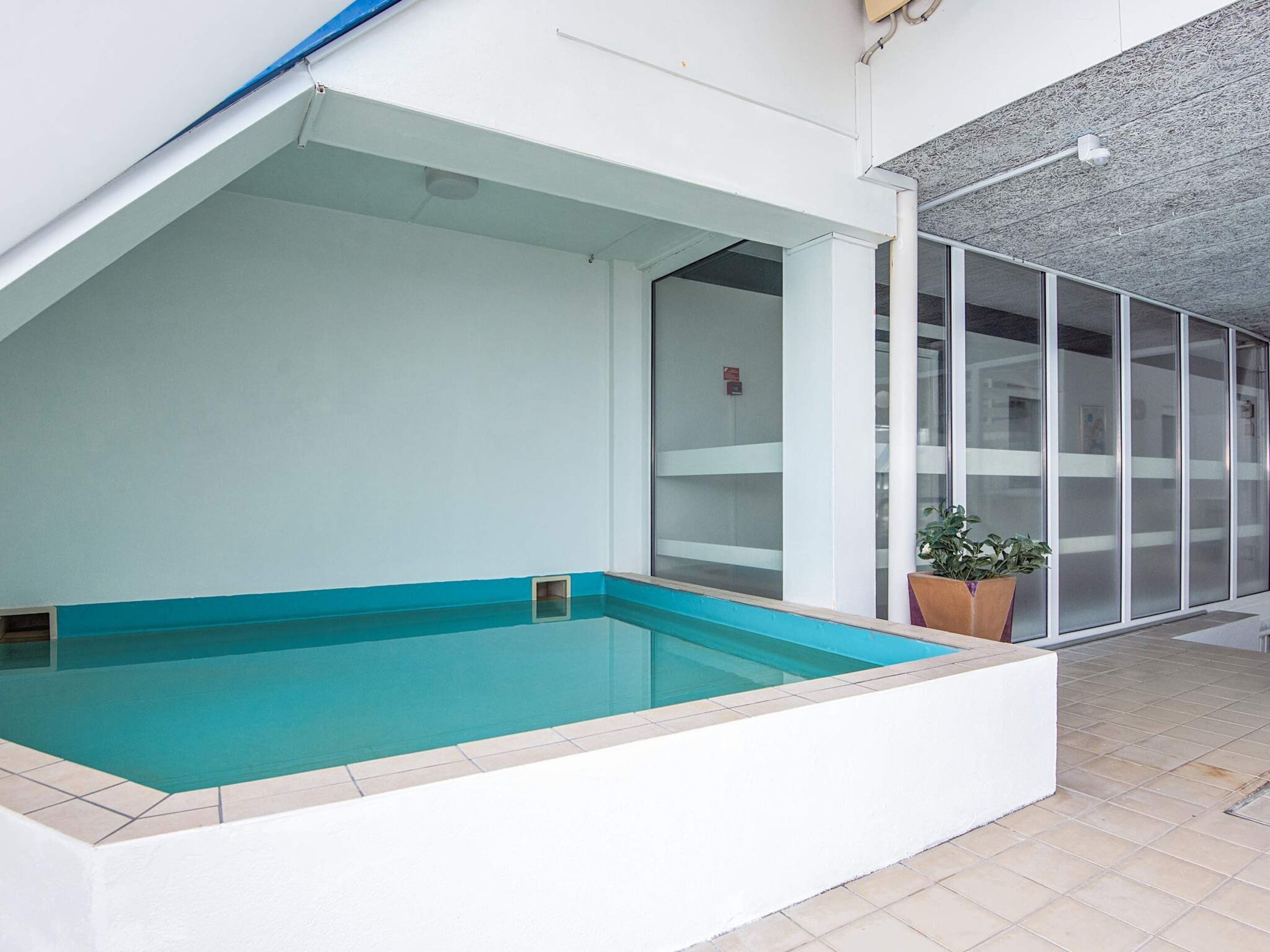 A swimming pool adjacent to a building with large windows and a tiled floor.