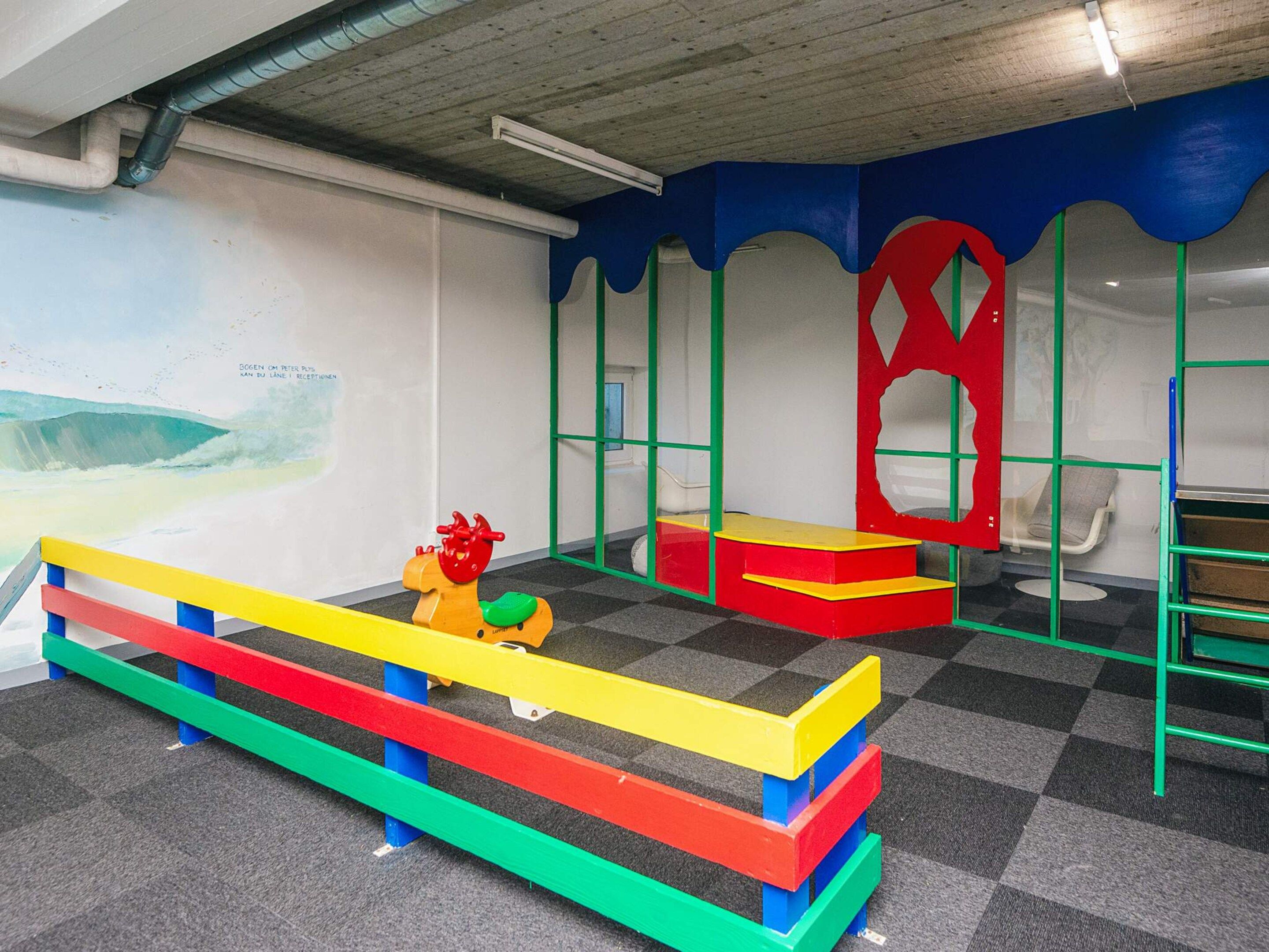 Ein Kinderspielbereich mit bunten Spielgeräten und einem Wandgemälde.