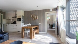 A modern kitchen with white cabinets, a wooden dining table, and a black coffee machine. - Bungalow in Limburg Near Nature Reserve (Stramproy)