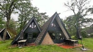 A modern, triangular-shaped building with a brick base and large windows, surrounded by a grassy area with outdoor seating. - Bungalow in Limburg Near Nature Reserve (Stramproy)