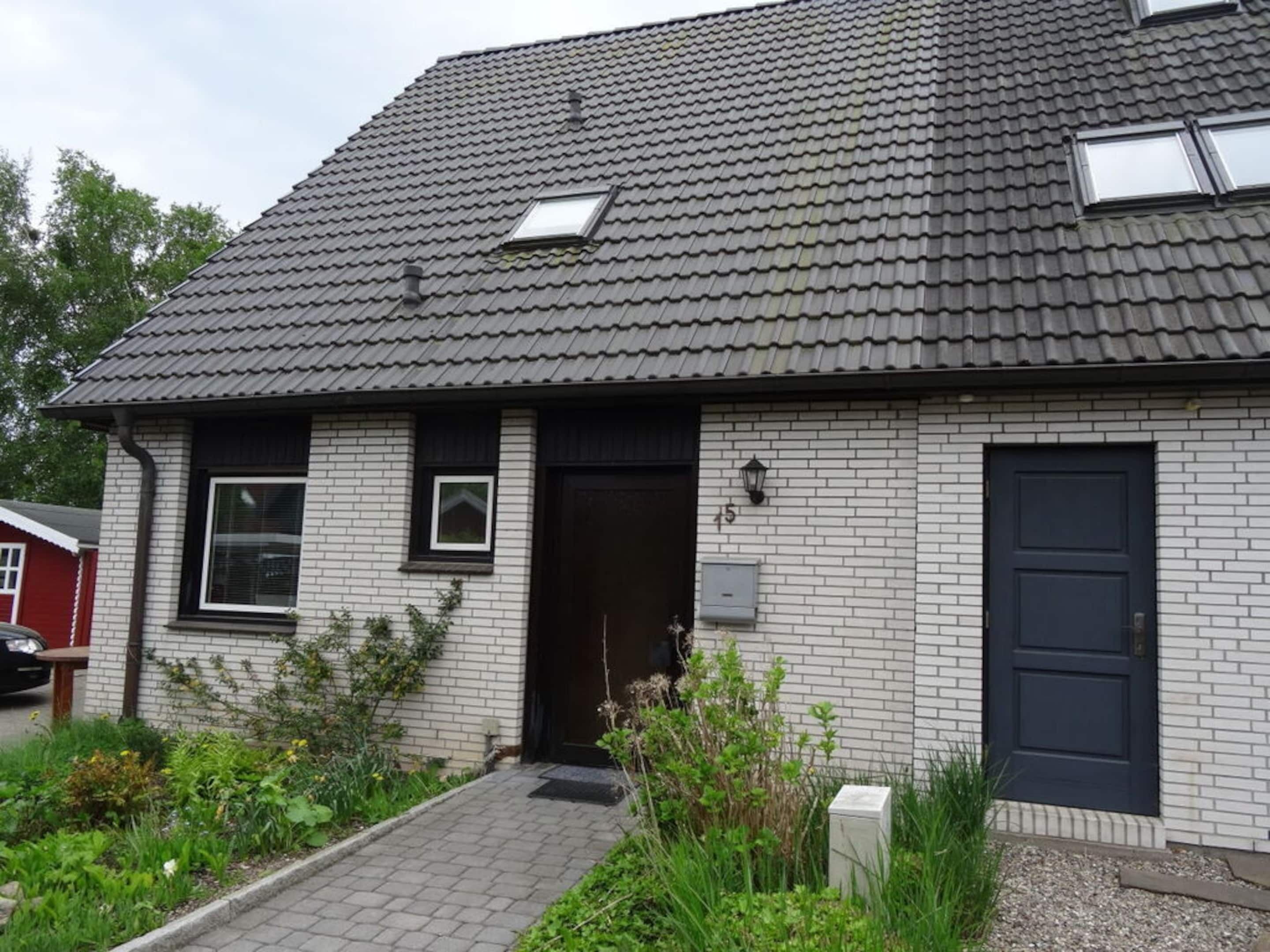 A two-story house with a dark roof, white brick exterior, and a small front garden.