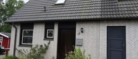 A two-story house with a dark roof, white brick exterior, and a small front garden.