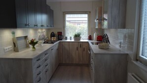 A compact kitchen with dark cabinets, a window with blinds, a countertop with a coffee maker, and a sink. - Anchorage Modern Retreat (Kappeln)