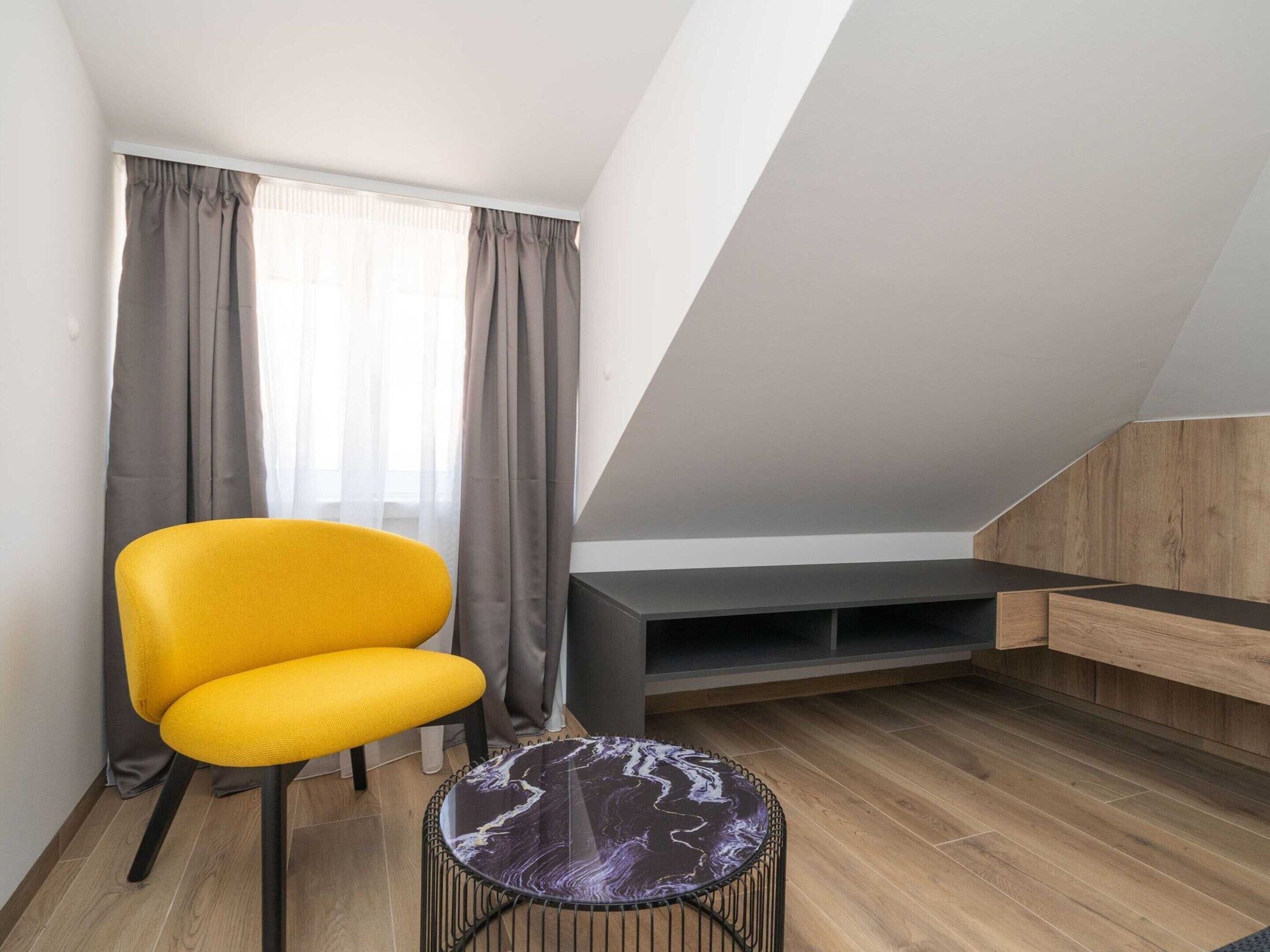 Una habitación moderna con una silla amarilla, una mesa redonda con un diseño parecido al mármol y un banco empotrado con acabados de madera.