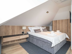 A modern bedroom with a sloped ceiling, a bed with white linens, a wooden headboard, and a bedside table with a lamp. - Apartments Villa Royale - One Bedroom Apartment With Sea View (Konavle)