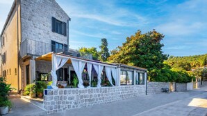 Un bâtiment en pierre doté d’un balcon et d’un espace extérieur aménagé avec des sièges, protégé par un auvent.