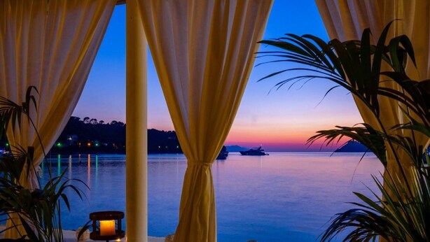 Une vue sur la mer depuis un balcon, avec des rideaux, une bougie et une chaise.