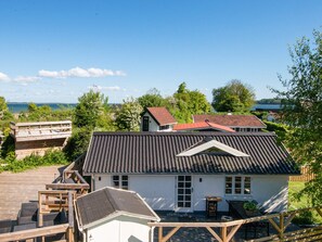 A two-story house with a sloped roof, a deck, and a view of the sea.