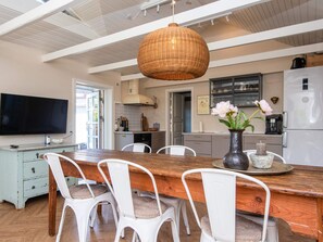 A modern kitchen with a wooden dining table, white chairs, a large hanging light fixture, and a refrigerator.