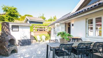 A patio with a stone fireplace, outdoor seating, and a view of a house with a tiled roof.