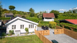 Un bâtiment blanc avec un toit rouge, entouré d’une clôture en bois et bordé d’une allée gravillonnée.