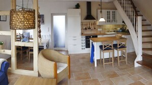 A spacious living area with a dining table, wicker chairs, a kitchen with white cabinets, and a wooden staircase. - WE Evening sun in the sun House (Kalkhorst)