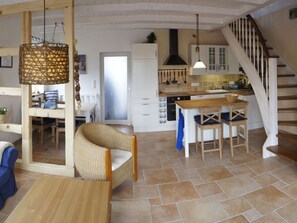 A spacious living area with a dining table, wicker chairs, a kitchen with white cabinets, and a wooden staircase. - WE Evening sun in the sun House (Kalkhorst)
