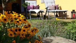 Un espace patio comprenant deux chaises longues, un mur jaune et un jardin agrémenté de tournesols et de lavande.