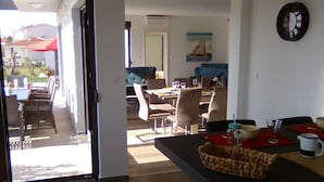 A modern kitchen with a central island, dining area with chairs and a table, and a view of the outdoor patio. - Charming Apartment in Istria (Vodnjan)