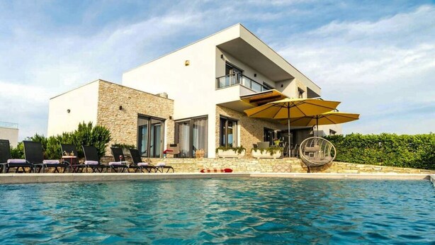 A modern building with a pool, lounge chairs, and umbrellas. - Charming Apartment in Istria (Vodnjan)