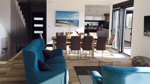 A modern living room with a blue sofa, a dining area with a table and chairs, and a kitchen in the background. - Charming Apartment in Istria (Vodnjan)