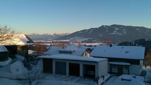 Ein Wohngebiet mit schneebedeckten Häusern, blauem Himmel und Bergen im Hintergrund.