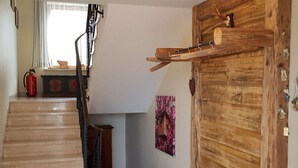 Eine Holztreppe führt zu einem Raum mit einer rustikalen Tür, einem Feuerlöscher und einem an der Wand befestigten Kleiderhaken.