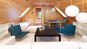 Ein gemütliches Dachzimmer mit Holzwänden, einem Schlafplatz auf Podest, einem Esstisch und zwei Stühlen.