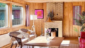 Ein gemütliches Zimmer mit Holzvertäfelung, einem Kamin aus Ziegelsteinen, Korbmöbeln und einem großen Fenster.