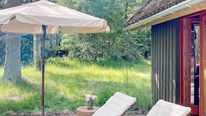 Ein sonniger Außenbereich mit Sitzgelegenheiten, zwei Lounge-Stühlen und einem Tisch, umgeben von üppigem Grün.