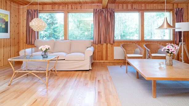 Ein gemütliches Blockhaushaus-Interieur mit einer Couch, einem Esstisch und Korbstühlen.