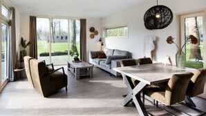 A spacious living room with a large dining table, comfortable seating, and a view of the outdoors. - Paviljoen 4 Personen (Zorgvlied)